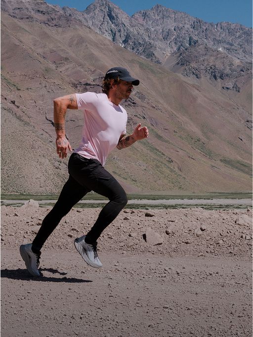 Person running on a rocky plain with mountains in the background, wearing Merrell running shoes.